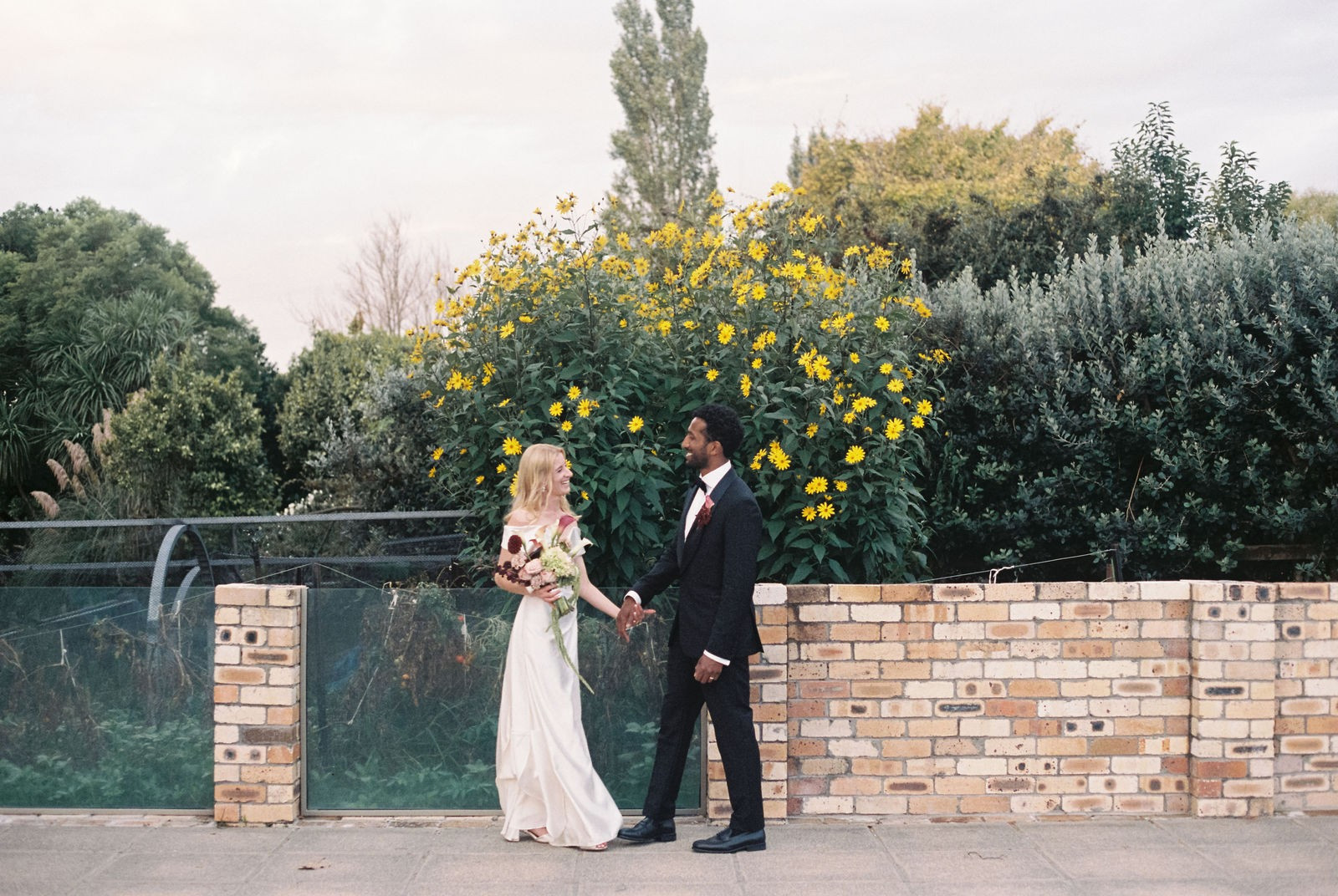 35mm film photograph of a couple by a flowering wall